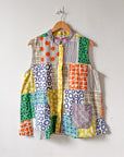 Colorful patchwork buttondown sleeveless shirt on a hanger against a white wall