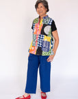 Woman wearing a colorful patchwork patterned shirt and blue pants on a white background