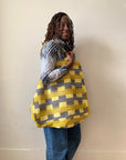 Person holding a yellow and black patterned bag against a plain background