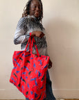 Person holding a red tote bag with cat pattern against a plain background