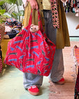 Person holding a red bag with animal patterns, wearing a yellow cardigan and blue jeans, in an indoor setting.