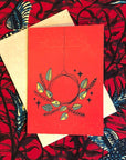Red colored greeting card with green and yellow wreath
