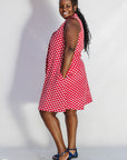 Model wearing red sleeveless dress with white dots.