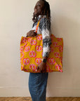 Person holding a yellow tote bag with red patterns against a plain background