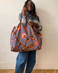 Person holding a large, patterned bag against a plain background