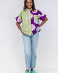Woman wearing a colorful shirt with green and purple patterns and light blue jeans on a white background