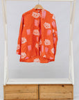 Orange shirt on a wooden and white rack with drawers against a white background