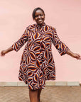Model wearing brown, orange, burgundy and white abstract print dress.