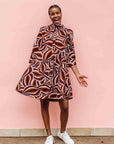 Model wearing brown, orange, burgundy and white abstract print dress.