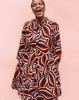 Model wearing brown, orange, burgundy and white abstract print dress.