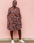 Model wearing brown, orange, burgundy and white abstract print dress.