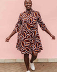 Model wearing brown, orange, burgundy and white abstract print dress.