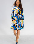 Model wearing blue dress with yellow, black, orange and white geometric print.