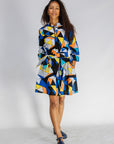 Model wearing blue dress with yellow, black, orange and white geometric print.