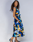 Model wearing blue dress with yellow, black, orange and white geometric print.