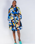 Model wearing blue dress with yellow, black, orange and white geometric print.