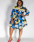 Model wearing blue dress with yellow, black, orange and white geometric print.