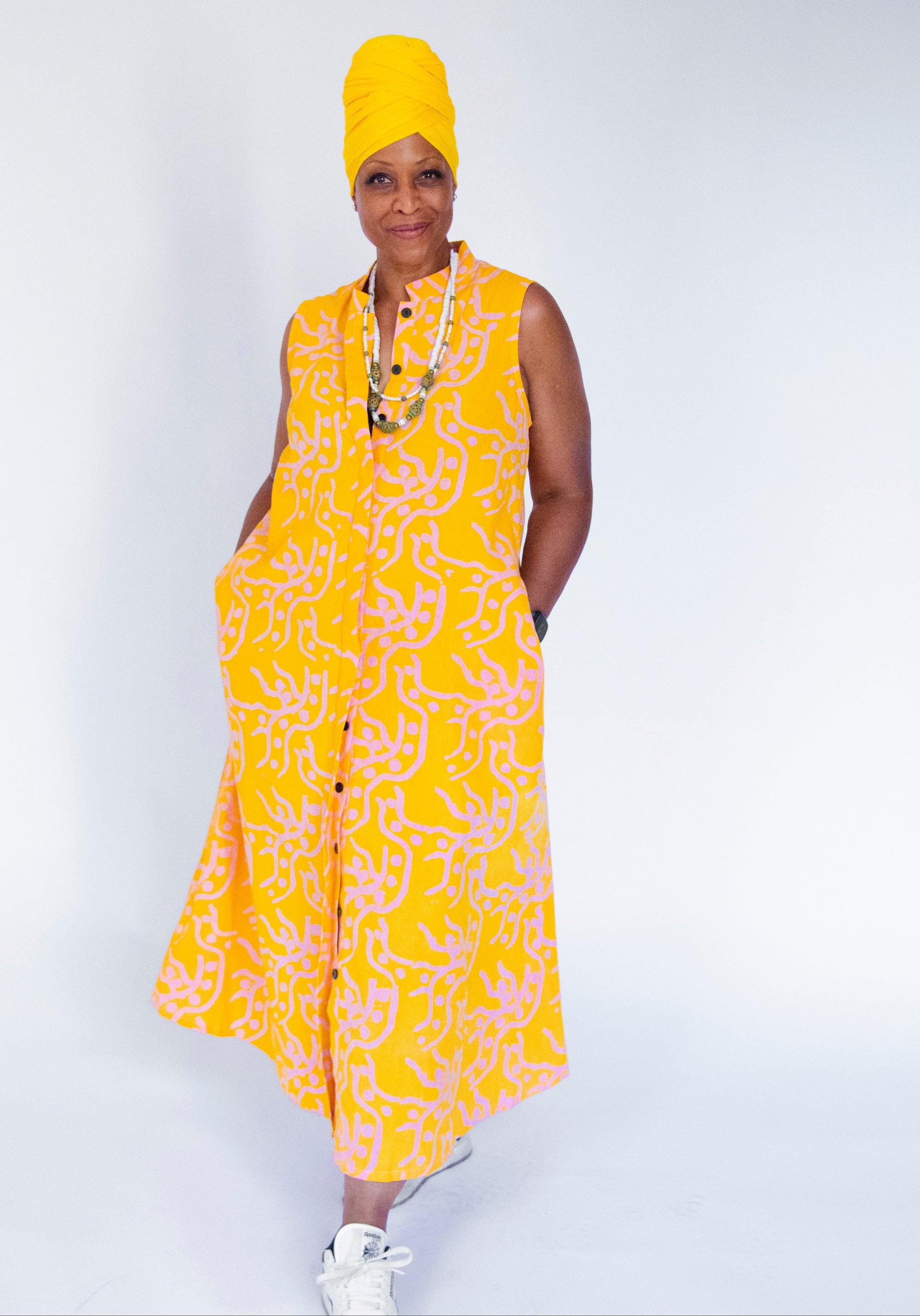 Model wearing yellow sleeveless dress with abstract pink print.