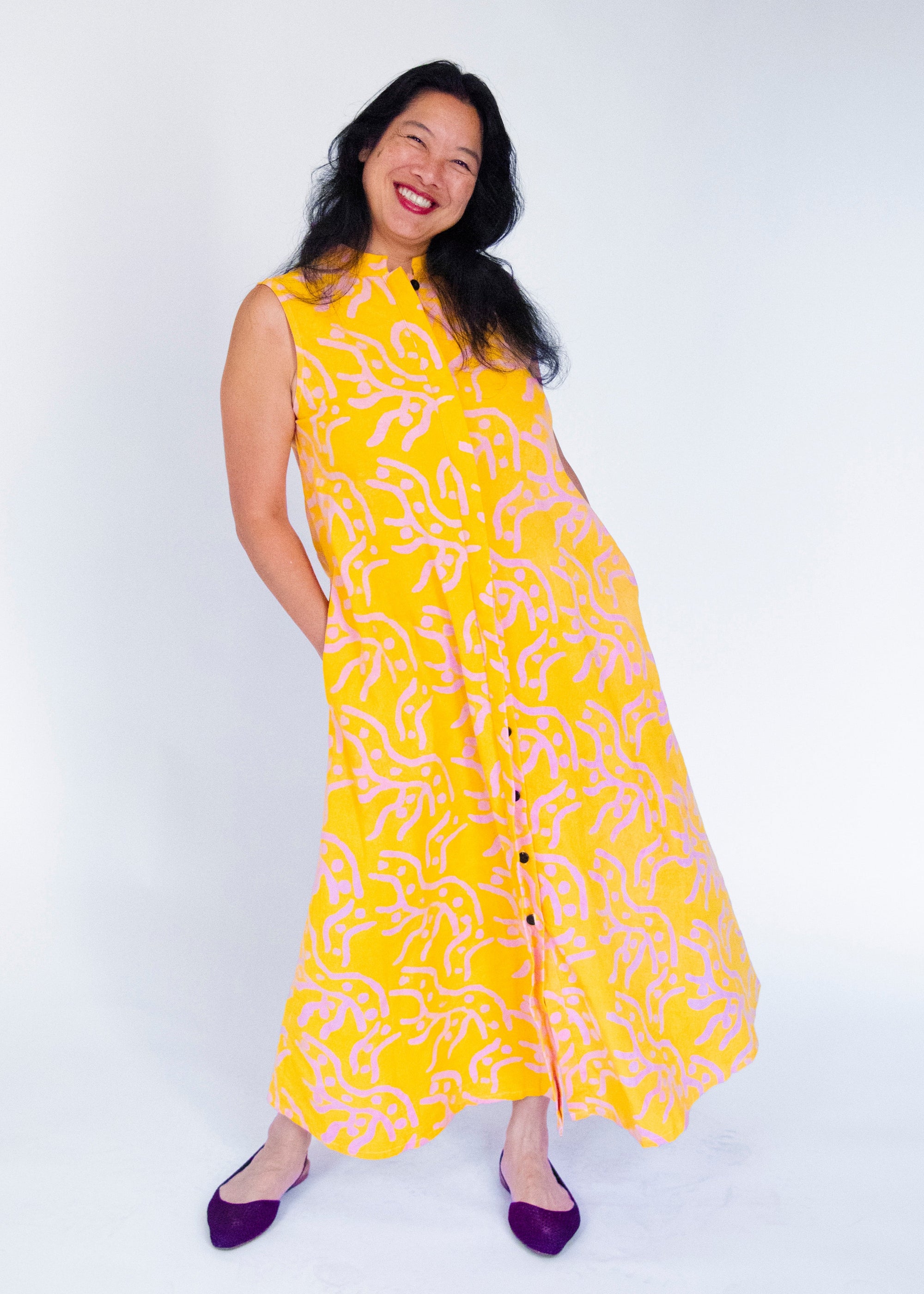 Model wearing yellow sleeveless dress with abstract pink print.