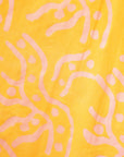 Close up display of yellow sleeveless dress with abstract pink print, fabric.