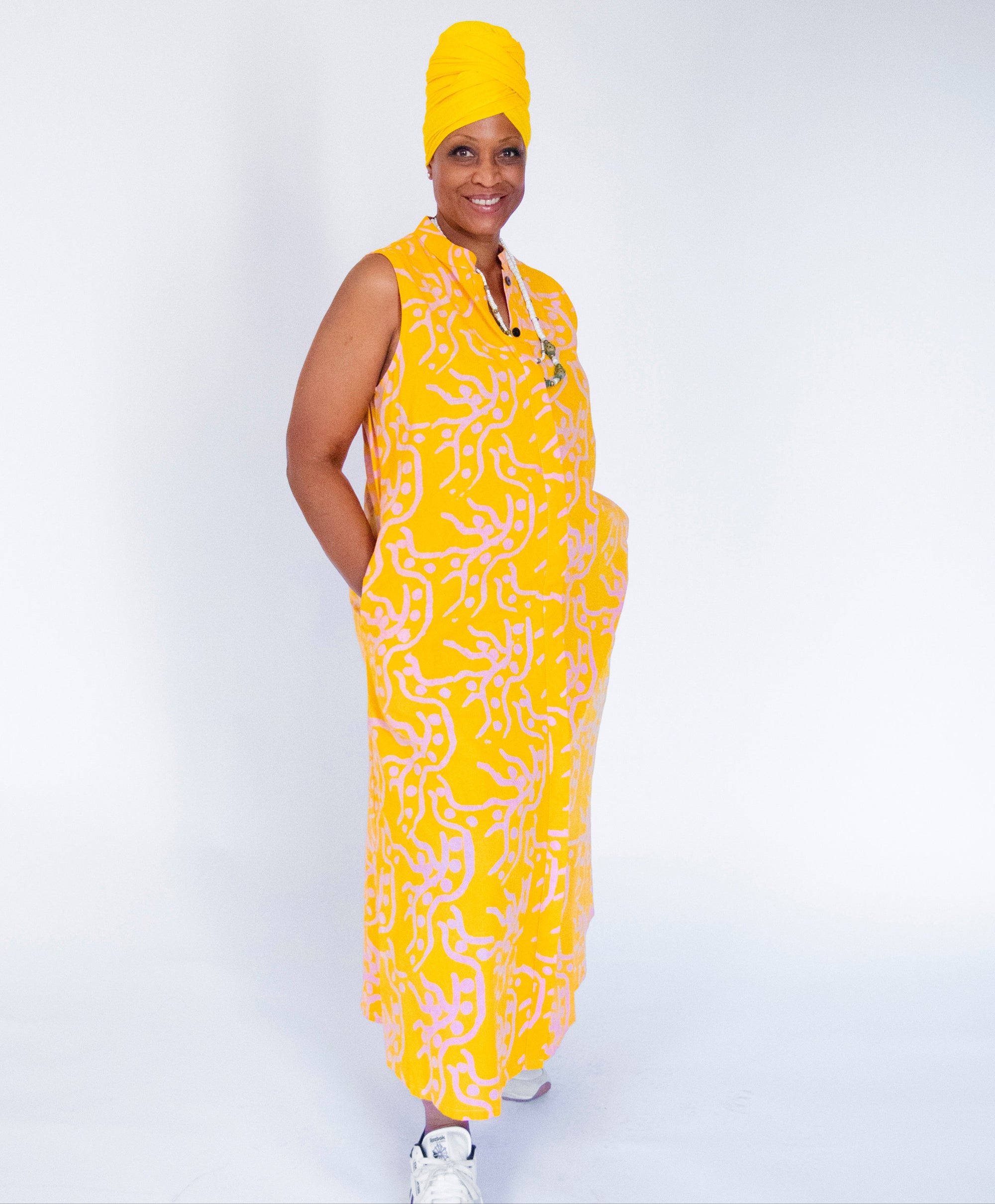 Model wearing yellow sleeveless dress with abstract pink print.