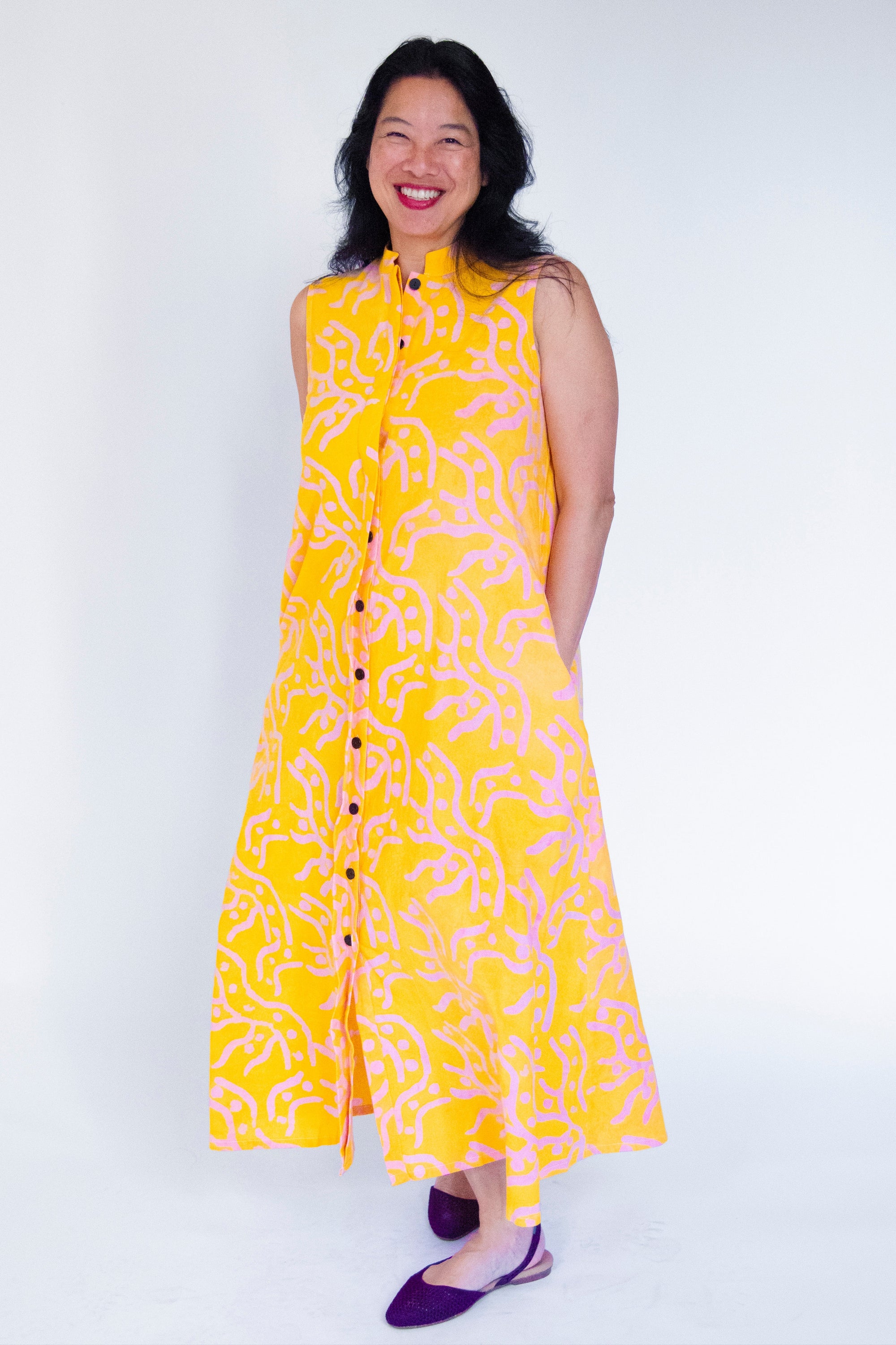 Model wearing yellow sleeveless dress with abstract pink print.