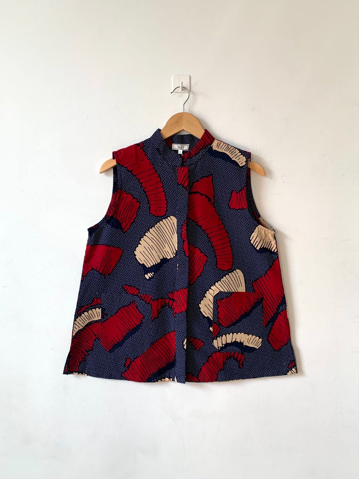Display of navy sleeveless shirt with red and beige abstract print.