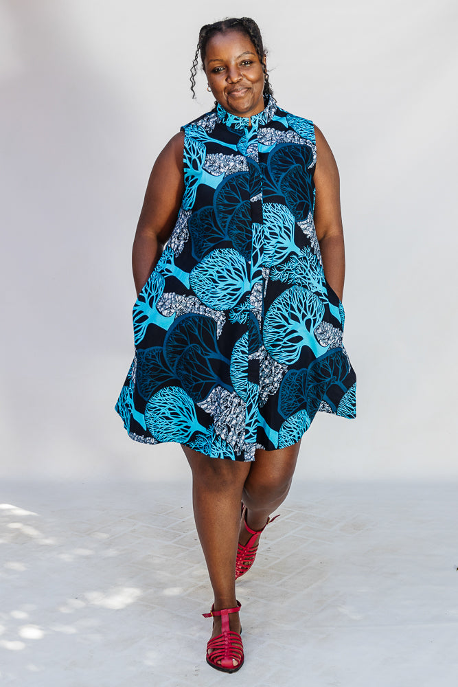 Model wearing sleeveless dress with blue tree print.