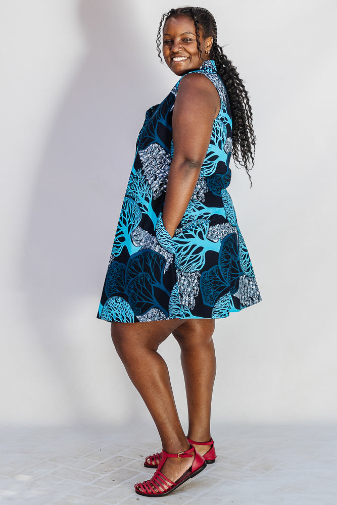 Model wearing sleeveless dress with blue tree print.