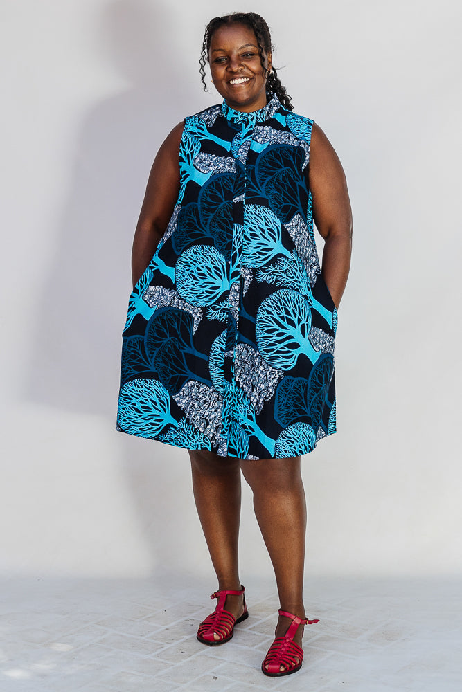 Model wearing sleeveless dress with blue tree print.