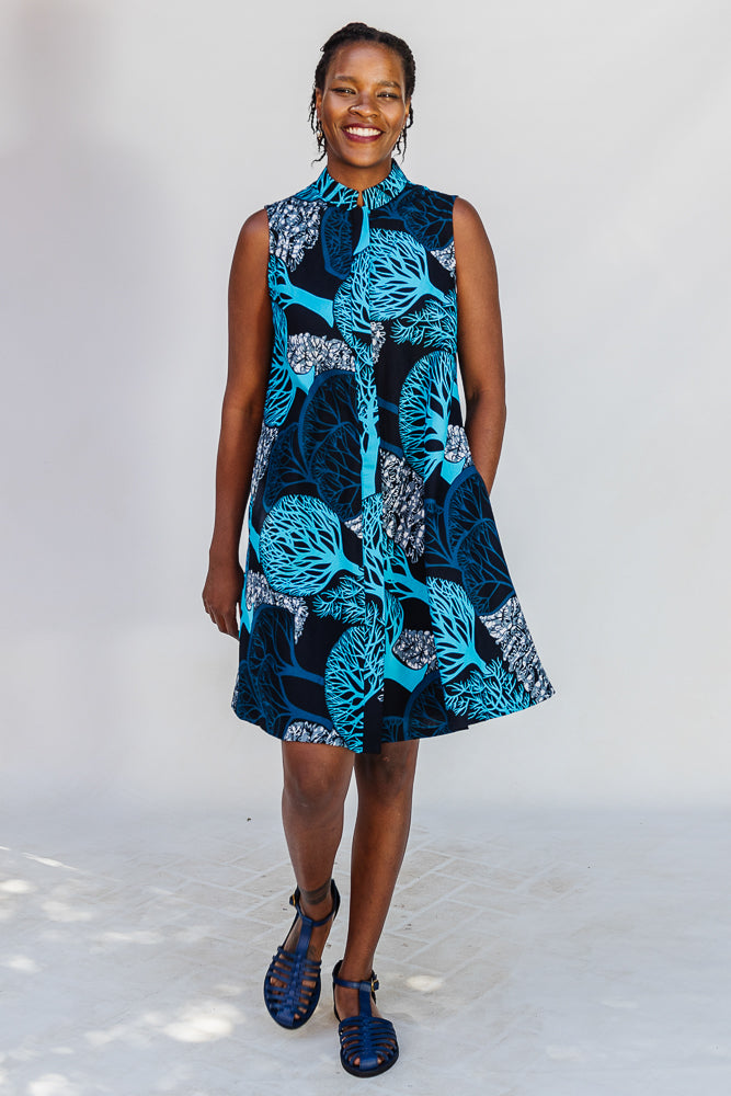 Model wearing sleeveless dress with blue tree print.