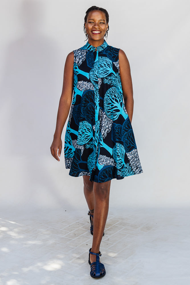 Model wearing sleeveless dress with blue tree print.