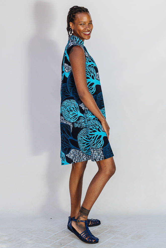 Model wearing sleeveless dress with blue tree print.