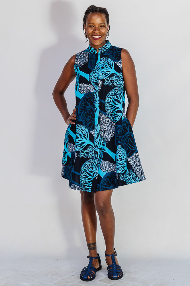 Model wearing sleeveless dress with blue tree print.
