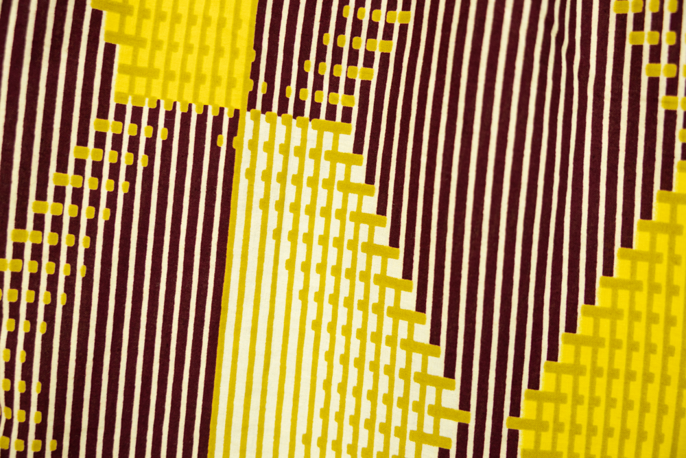 Close up display of Yellow, Maroon Brown, Mustard Green and Pale Yellow abstract print shirt, fabric.