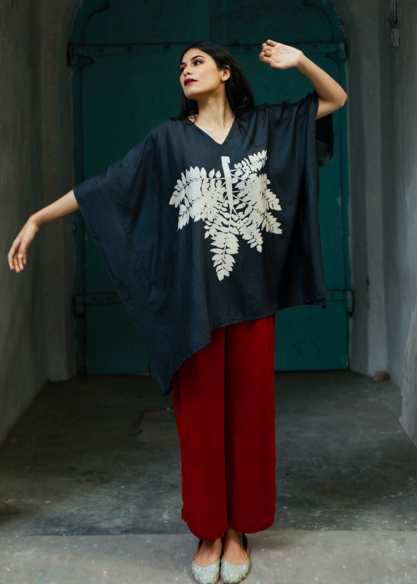 A person wearing a black kaftan with geometric patterns, standing in front of a blue door.