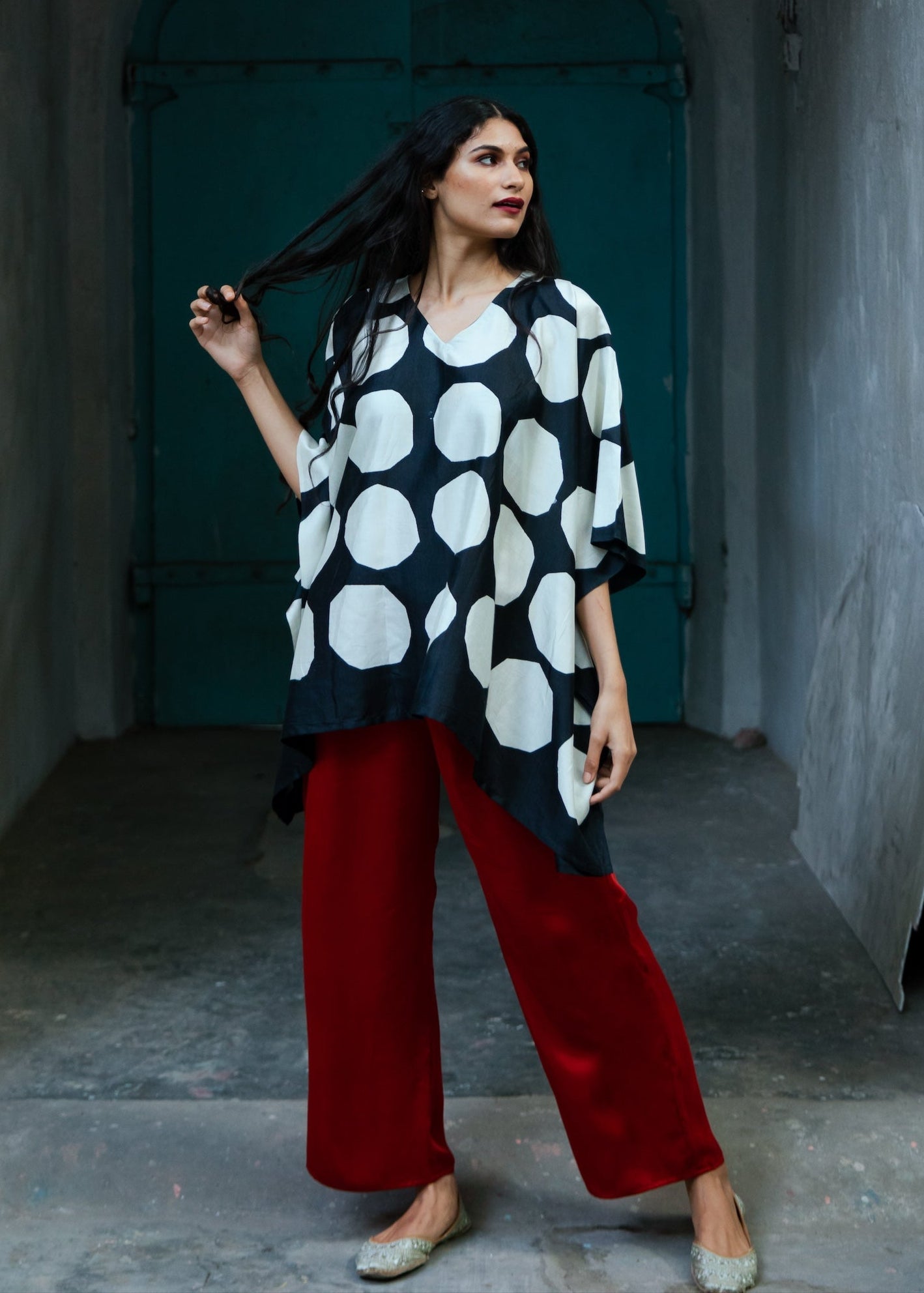 A person wearing a white kaftan with geometric patterns, standing in front of a blue door.
