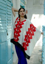 A person wearing a white kaftan with red geometric patterns, standing in front of a blue door.