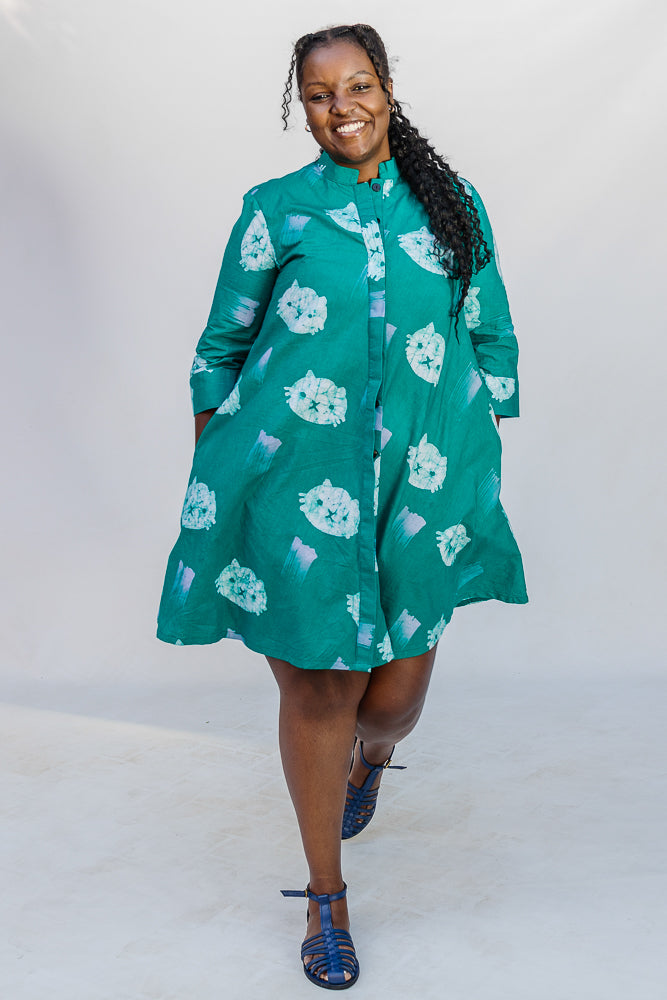 Model wearing teal dress with white cat print.