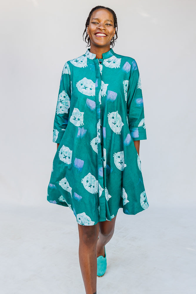 Model wearing teal dress with white cat print.