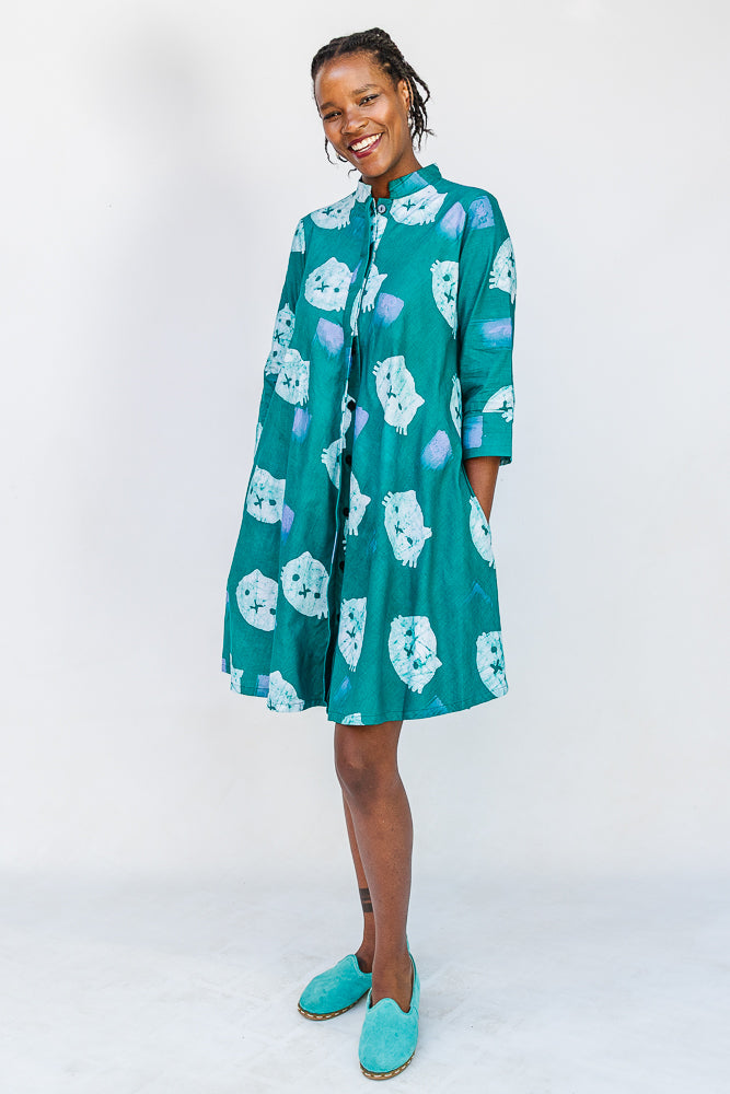 Model wearing teal dress with white cat print.