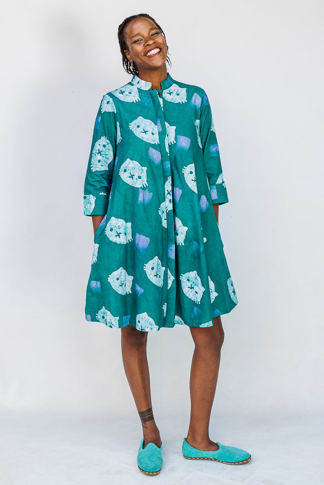 Model wearing teal dress with white cat print.