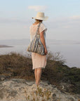 Person standing on a rocky outcrop overlooking a body of water with a hat and dress.