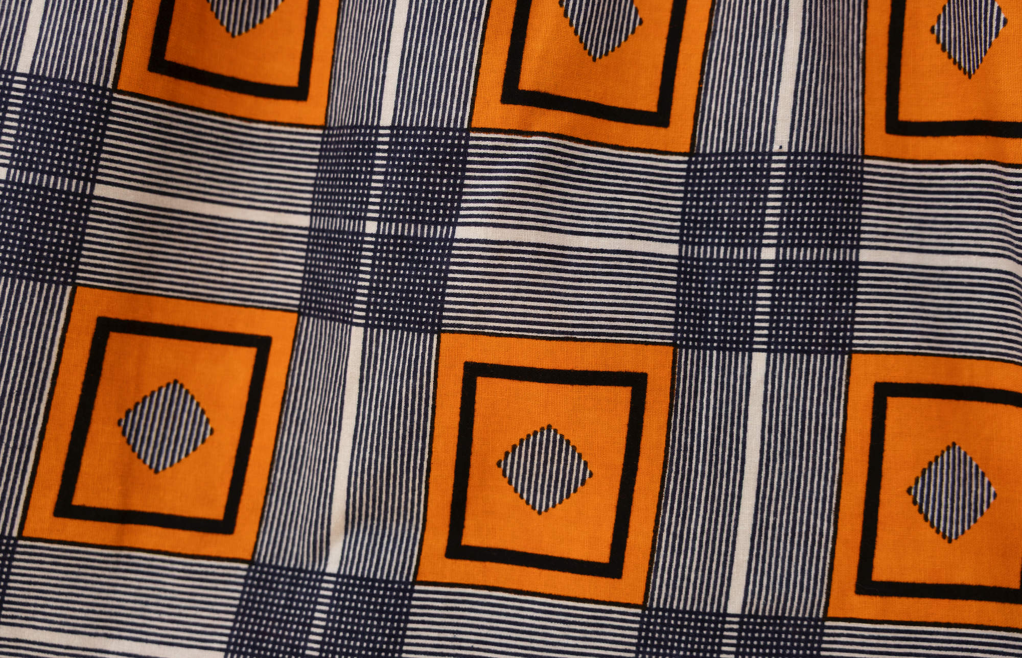 Close up display of orange, navy and white geometric print shirt, fabric.