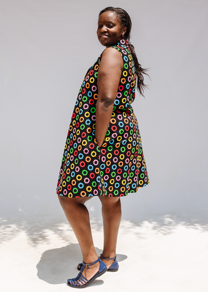 Model wearing black sleeveless dress with rainbow circle print.