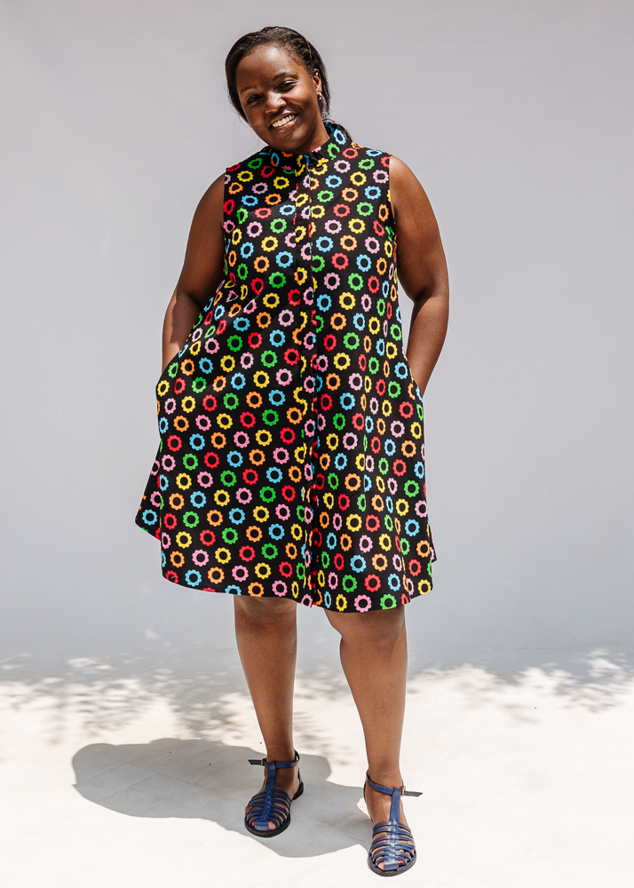 Model wearing black sleeveless dress with rainbow circle print.