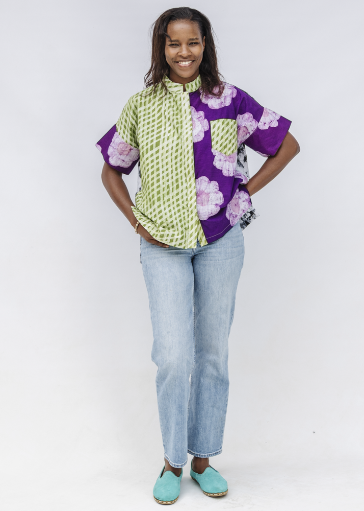 Woman wearing a colorful shirt with green and purple patterns and light blue jeans on a white background