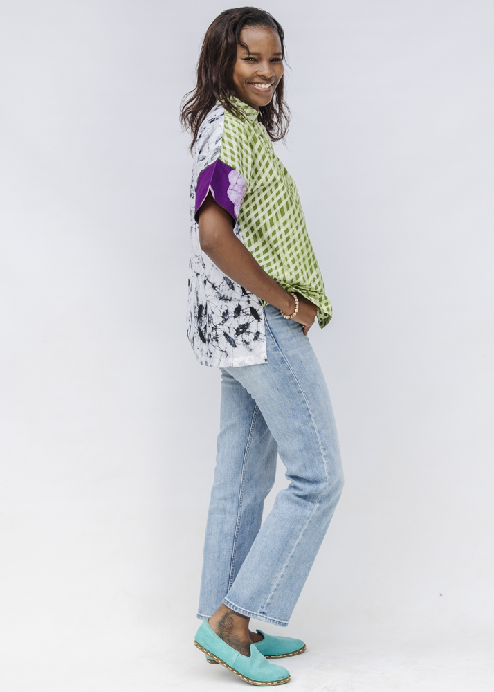 Woman wearing a patterned top, jeans, and turquoise shoes on a white background