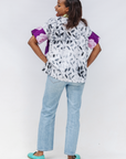Person wearing a patterned blouse with purple sleeves and light blue jeans on a white background