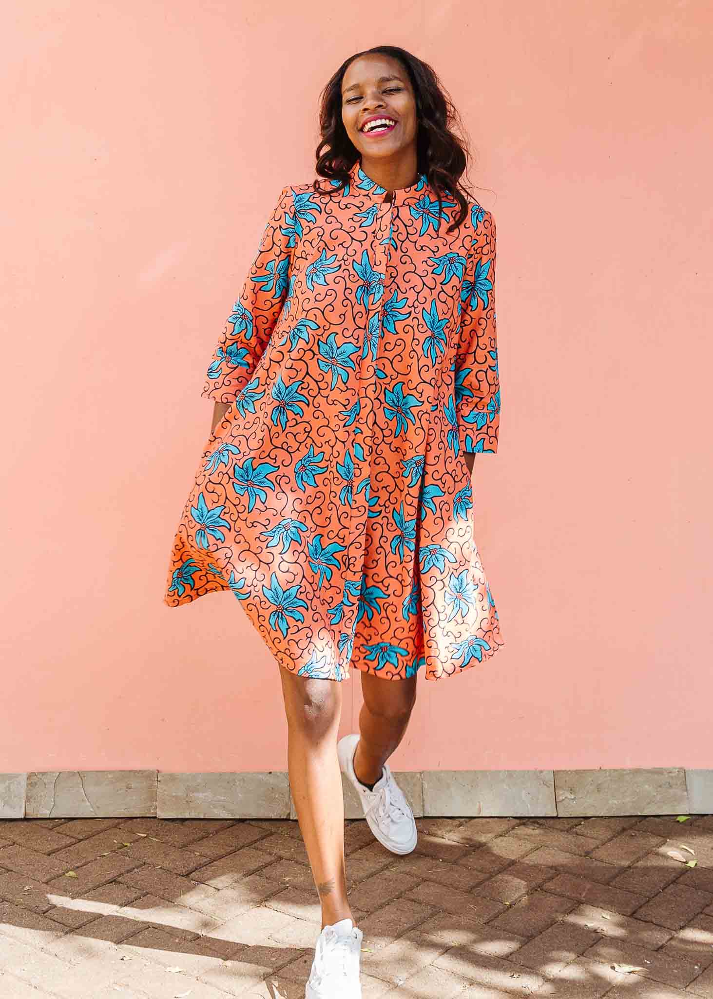 Model wearing orange dress with teal floral print.